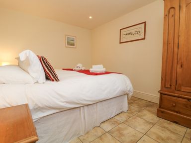 A bedroom with a bed with white sheets and red runner next to a wooden wardrobe and bedside table at Byre in Lostwithiel