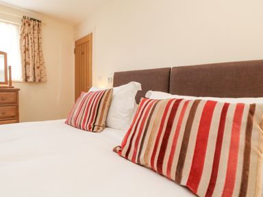A bedroom with a bed with striped pillows and white sheets near a wooden dresser with a mirror at Byre in Lostwithiel