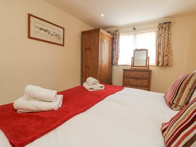 A bedroom with a bed, folded towels, a wooden wardrobe, a dresser with a mirror, and a window with curtains at Byre in Lostwithiel