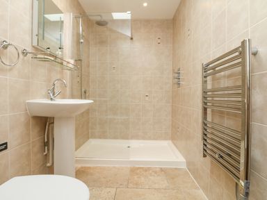 A bathroom with a sink shower area with glass partition and towel heater at Byre in Lostwithiel