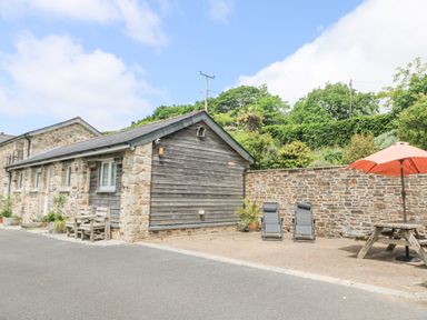 An outdoor patio area with two reclining chairs a wooden picnic table with an orange umbrella next to a stone and wood building at Byre in Lostwithiel