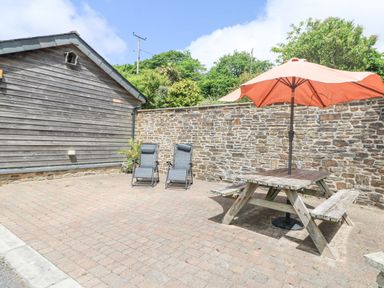 An outdoor patio area with two reclining chairs a wooden picnic table with an orange umbrella and a wooden shed at Byre in Lostwithiel