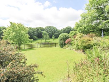 A garden with a lawn and various bushes and trees behind a wooden fence at Byre in Lostwithiel
