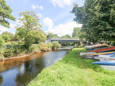 A river flowing under a bridge with boats lined up on the grassy bank at Byre in Lostwithiel