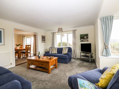 A living room with blue sofas a wooden coffee table and a television at Bethany Bay View in Holywell Bay
