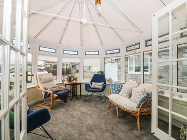 A conservatory with three chairs a small table and cushions at Bethany Bay View in Holywell Bay