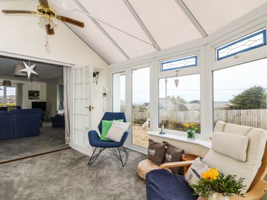 A sunroom with blue and beige chairs and cushions with a view of a garden at Bethany Bay View in Holywell Bay