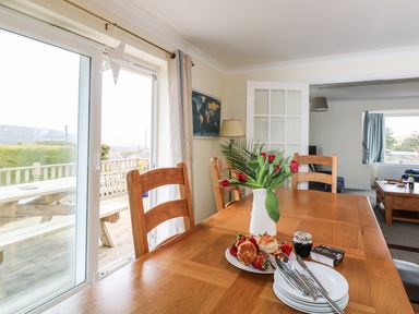 A dining room table with a vase of tulips plates and food next to glass sliding doors at Bethany Bay View in Holywell Bay