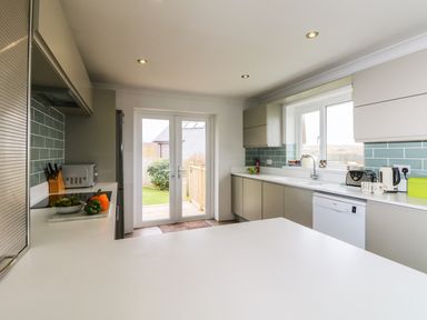 A kitchen with cabinets sink dishwasher and double doors leading to a garden at Bethany Bay View in Holywell Bay