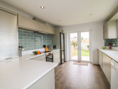 A kitchen with white countertops green tiled backsplash and wooden floor at Bethany Bay View in Holywell Bay