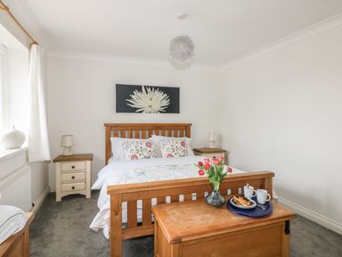 A bedroom with wooden bed frame bedside tables with lamps a chest at the foot of the bed with flowers and breakfast tray Bethany Bay View in Holywell Bay