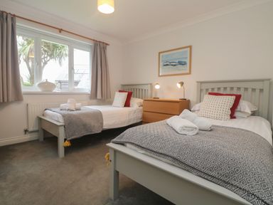 A bedroom with two single beds a wooden dresser and a window with curtains at Bethany Bay View in Holywell Bay