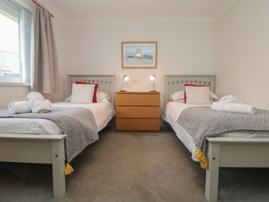 A bedroom with two single beds and a wooden chest of drawers with lamps at Bethany Bay View in Holywell Bay