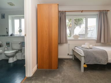 A bedroom with a bed and towels near a window and an adjacent bathroom with a toilet at Bethany Bay View in Holywell Bay