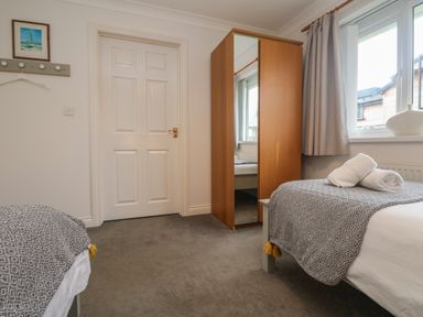 A bedroom with two single beds a wooden wardrobe and a window at Bethany Bay View in Holywell Bay