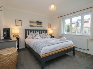 A bedroom with a bed with floral pillows bedside tables with lamps a window and a TV at Bethany Bay View in Holywell Bay