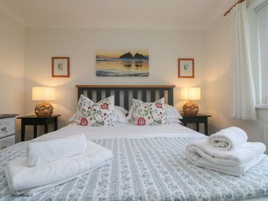 A bedroom with a bed with floral pillows and folded towels on it at Bethany Bay View in Holywell Bay
