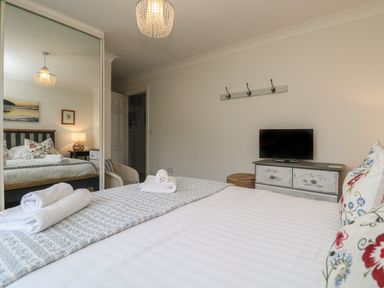 A bedroom with a bed with folded towels on it a mirrored wardrobe a television on a chest of drawers and a wall-mounted coat rack at Bethany Bay View in Holywell Bay