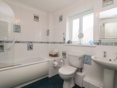 A bathroom with a bathtub toilet and sink featuring nautical themed tiles at Bethany Bay View in Holywell Bay
