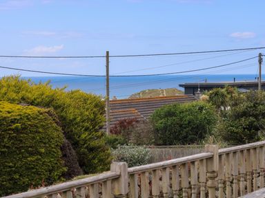 A garden with bushes and a wooden fence overlooking rooftops and the sea at Bethany Bay View in Holywell Bay