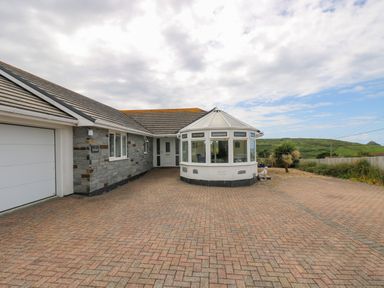 A driveway in front of a house with a garage and a conservatory with hills in the background at Bethany Bay View in Holywell Bay