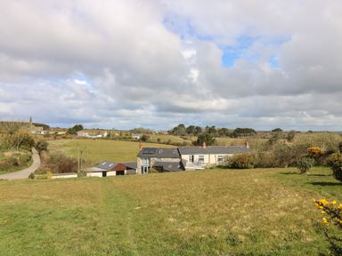 A rural landscape with a farmhouse and outbuildings surrounded by fields and trees at Mynheer Farm Barn Nr Portreath