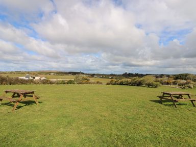 A grassy field with two wooden picnic tables and a cloudy sky at Mynheer Farm Barn Nr Portreath