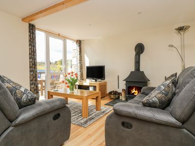 A living room with two gray sofas a wooden coffee table with flowers a television and a wood burning stove at Mynheer Farm Barn Nr Portreath