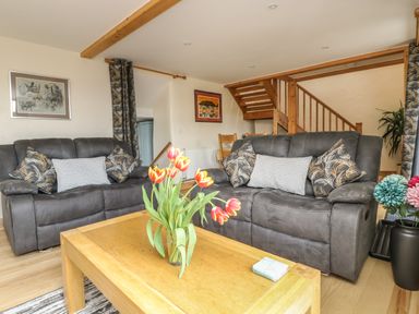 A living room with two dark sofas a wooden coffee table with flowers and stairs in the background at Mynheer Farm Barn Nr Portreath