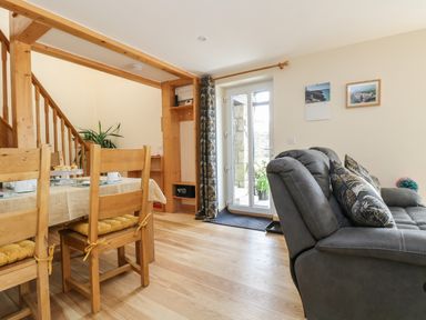 A dining area with wooden chairs and table next to a gray sofa and glass door at Mynheer Farm Barn Nr Portreath