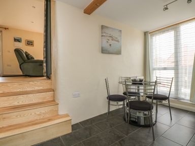 A dining area with a round glass table and four metal chairs next to a window with curtains at Mynheer Farm Barn Nr Portreath