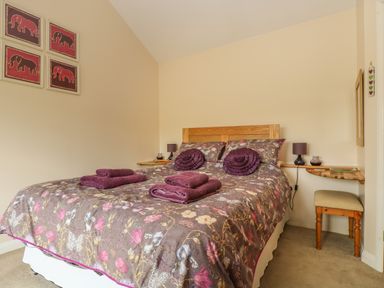 A bedroom with a double bed floral bedding purple towels and pillows bedside table with lamp and a small stool at Mynheer Farm Barn Nr Portreath