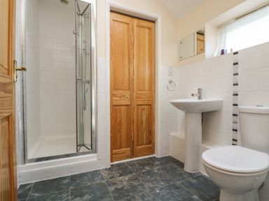 A bathroom with a shower, wooden closet doors, a pedestal sink, and a toilet at Mynheer Farm Barn Nr Portreath