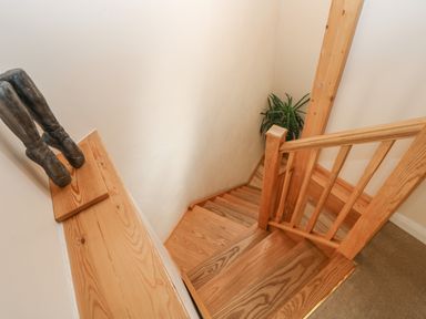A wooden staircase with railing a plant at the bottom and a sculpture of legs on a wooden shelf at Mynheer Farm Barn Nr Portreath