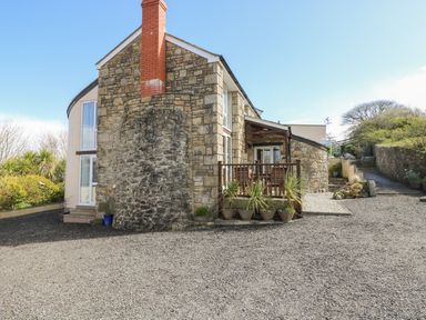 A stone house with a chimney and a small porch with plants in pots at Mynheer Farm Barn in Nr Portreath