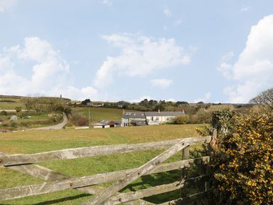 A countryside landscape with grassy fields a wooden gate a house and a hedgerow at Mynheer Farm Barn Nr Portreath