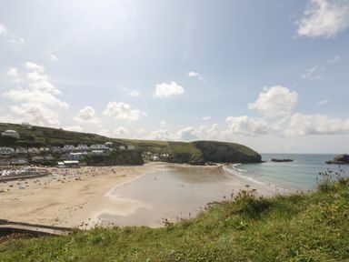 A beach with people and houses along the shore and hills in the background at Mynheer Farm Barn Nr Portreath