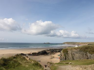 A beach with people walking and relaxing near rocks and grassy cliffs at Mynheer Farm Barn Nr Portreath