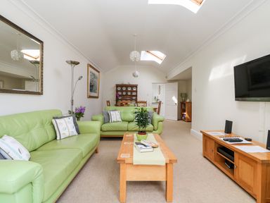 A living room with green sofas a wooden coffee table and a wall mounted television at Seabien in Falmouth