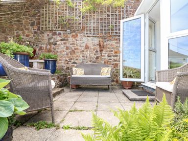 An outdoor patio with wicker chairs and a loveseat against a stone wall with potted plants at Seabien in Falmouth
