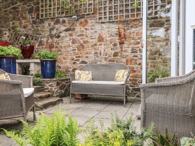 An outdoor patio area with wicker chairs and a loveseat in front of a stone wall with potted plants at Seabien in Falmouth