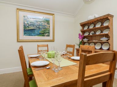 A dining room with a wooden table set for six and a wooden plate rack with plates at Seabien in Falmouth