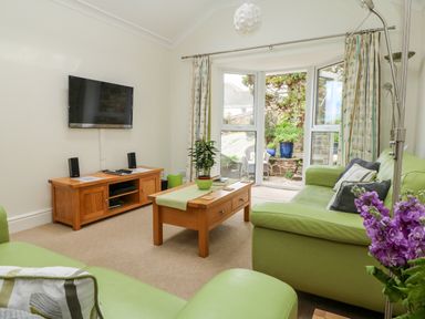 A living room with green sofas a wooden coffee table a wooden TV stand and a wall mounted TV at Seabien in Falmouth