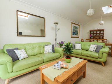 A living room with two green sofas a wooden coffee table with books and a plant a dining table in the background at Seabien in Falmouth