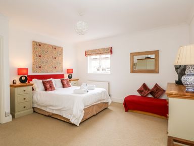 A bedroom with a double bed, bedside tables with lamps, a window, a bench with cushions, a dresser with a lamp, and a wall mirror at Seabien in Falmouth
