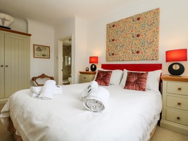 A bedroom with a bed with white bedding and rolled towels two bedside tables with lamps a wardrobe and a door leading to a bathroom at Seabien in Falmouth