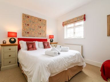 A bedroom with a double bed with white bedding red cushions and bedside tables with lamps at Seabien in Falmouth