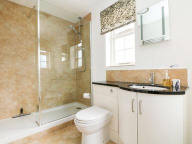 A bathroom with a shower enclosure a toilet and a sink with a black countertop and white cabinets at Seabien in Falmouth