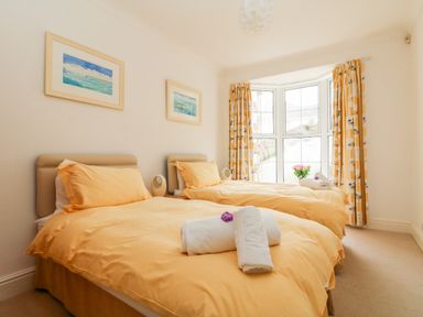A bedroom with two single beds with yellow bedding and white towels by a bay window with patterned curtains at Seabien in Falmouth