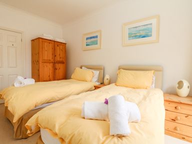 A bedroom with two single beds with yellow bedding and a wooden wardrobe and dresser at Seabien in Falmouth